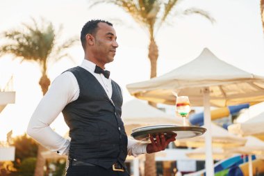 Elinde bir düzenle. Resmi kıyafetli zenci garson güneşli bir günde iş yerinde..