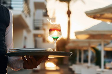 İçkinin yakın görüntüsü. Resmi kıyafetli zenci garson güneşli bir günde iş yerinde..