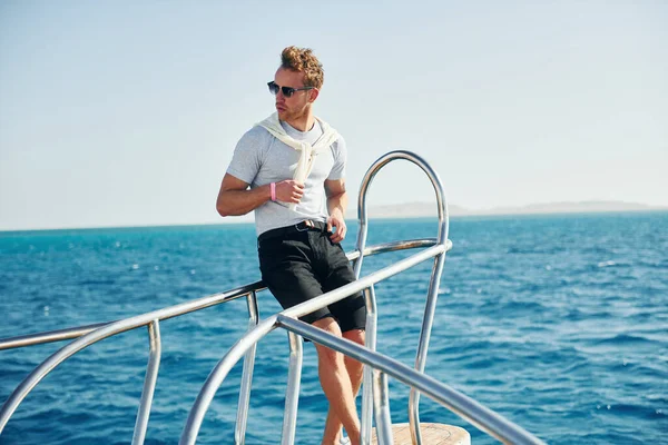 Kamera için poz vermek. Genç erkek turist denizdeki yatta. Tatil kavramı.