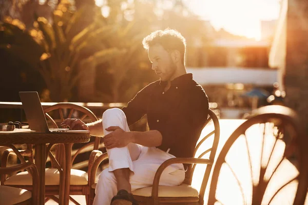 Masanın yanında oturuyor. Genç adam güneşli bir günde dışarıda. Tatil kavramı.