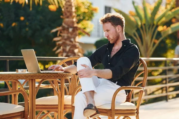 Masanın yanında oturuyor. Genç adam güneşli bir günde dışarıda. Tatil kavramı.