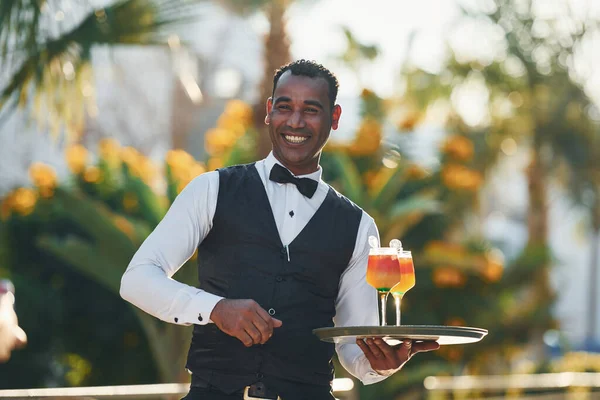 Kokteyl tutuyor. Resmi kıyafetli zenci garson güneşli bir günde iş yerinde..
