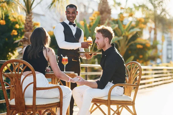 Garson tarafından servis ediliyor. Mutlu genç çift tatilde birlikte. Güneşli bir günde açık havada..