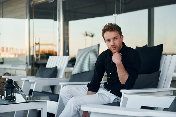 Masanın yanında oturuyor. Genç adam güneşli bir günde dışarıda. Tatil kavramı.