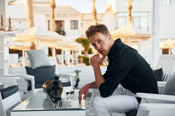 Masanın yanında oturuyor. Genç adam güneşli bir günde dışarıda. Tatil kavramı.