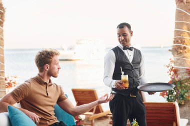 Garson tarafından servis ediliyor. Genç adam güneşli bir günde dışarıda. Tatil kavramı.