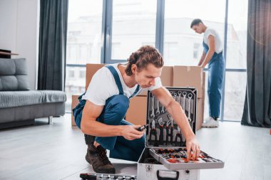 Ekipmanlı çanta. İçeride çalışan mavi üniformalı iki genç nakliyeci..