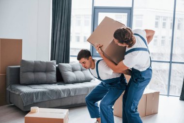 Ağır kutular. İçeride çalışan mavi üniformalı iki genç nakliyeci..