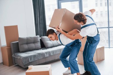 Ağır kutular. İçeride çalışan mavi üniformalı iki genç nakliyeci..