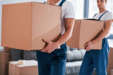 Ellerinde kutularla. İçeride çalışan mavi üniformalı iki genç nakliyeci..