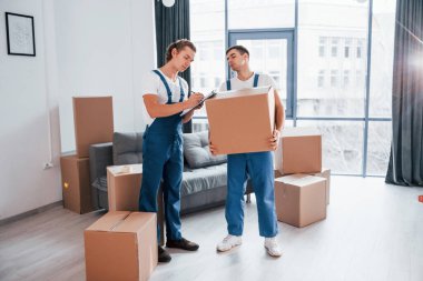 İçinde belge olan bir not defteri tutuyor. İçeride çalışan mavi üniformalı iki genç nakliyeci..