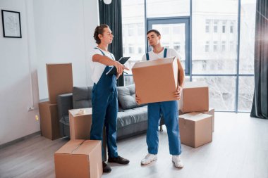 İçinde belge olan bir not defteri tutuyor. İçeride çalışan mavi üniformalı iki genç nakliyeci..