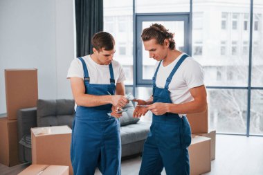 Param var. İçeride çalışan mavi üniformalı iki genç nakliyeci..