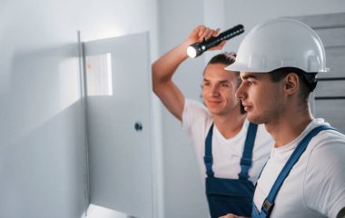 İki genç elektrikçi içeride birlikte çalışıyor. El feneri kullanıyor..