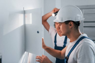 İki genç elektrikçi içeride birlikte çalışıyor. El feneri kullanıyor..