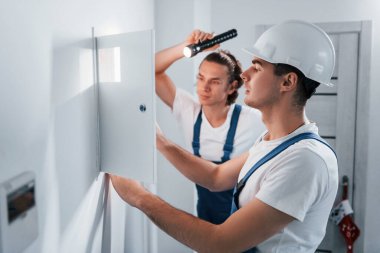 İki genç elektrikçi içeride birlikte çalışıyor. El feneri kullanıyor..