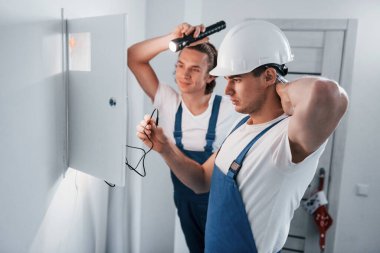İki genç elektrikçi içeride birlikte çalışıyor. El feneri kullanıyor..