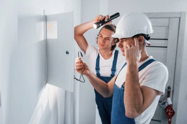 İki genç elektrikçi içeride birlikte çalışıyor. El feneri kullanıyor..