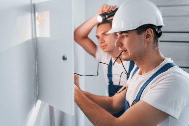 İki genç elektrikçi içeride birlikte çalışıyor. El feneri kullanıyor..