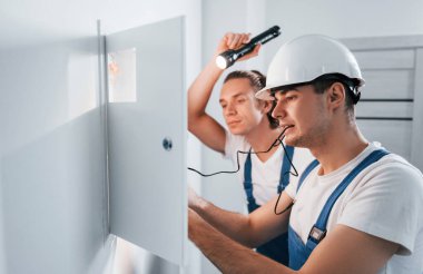 İki genç elektrikçi içeride birlikte çalışıyor. El feneri kullanıyor..