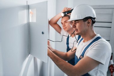 İki genç elektrikçi içeride birlikte çalışıyor. El feneri kullanıyor..
