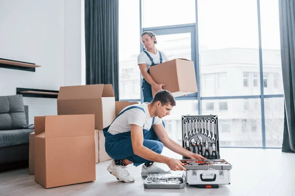 Davadaki aletleri kullanıyor. İçeride çalışan mavi üniformalı iki genç nakliyeci..