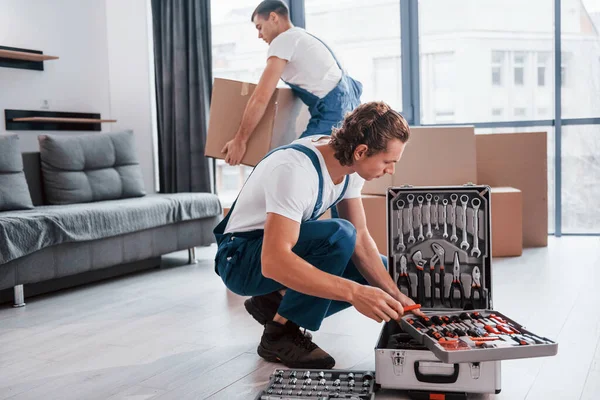 Davadaki aletleri kullanıyor. İçeride çalışan mavi üniformalı iki genç nakliyeci..