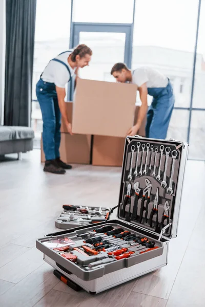 Case Equipment Two Young Movers Blue Uniform Working Indoors Room — Zdjęcie stockowe