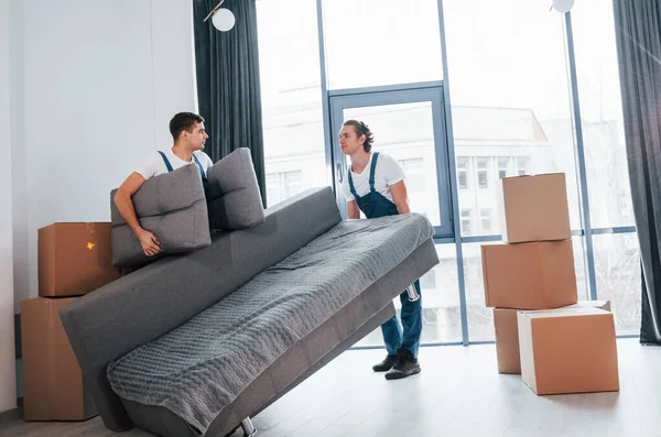 Ağır kanepe taşıyor. İçeride çalışan mavi üniformalı iki genç nakliyeci..