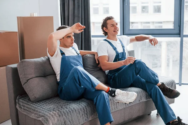 Sitting Sofa Tired Taking Break Two Young Movers Blue Uniform — Foto de Stock