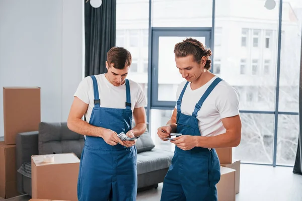 Param var. İçeride çalışan mavi üniformalı iki genç nakliyeci..