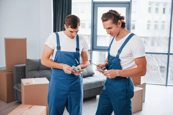 Param var. İçeride çalışan mavi üniformalı iki genç nakliyeci..