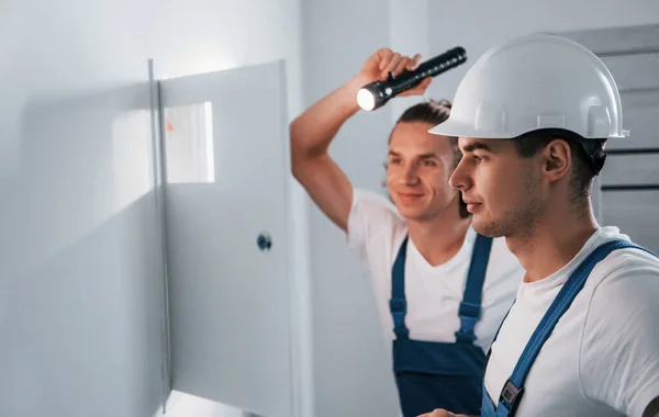 Two Young Male Electricians Works Indoors Together Using Flashlight — Zdjęcie stockowe