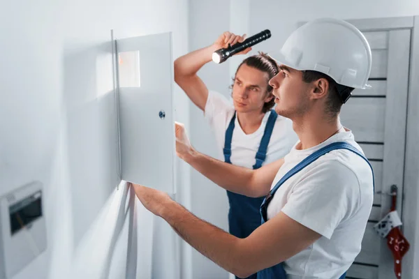 Two Young Male Electricians Works Indoors Together Using Flashlight — Zdjęcie stockowe