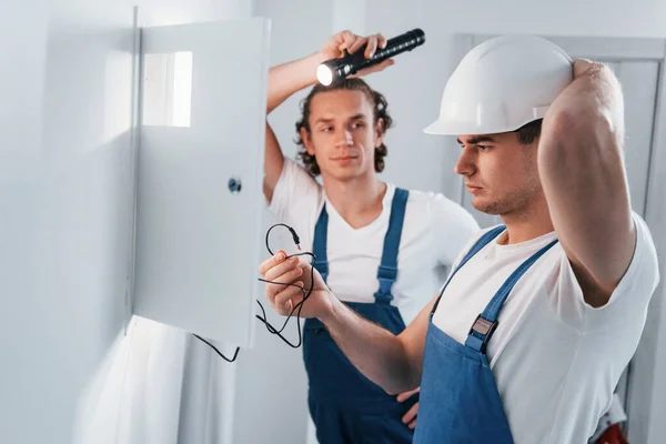 Two Young Male Electricians Works Indoors Together Using Flashlight — Zdjęcie stockowe