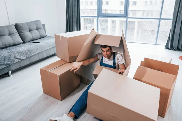 Mavi üniformalı genç erkek taşıyıcı kutularla yerde yatıyor..