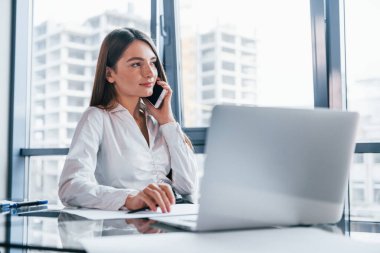 Telefonla konuş. Beyaz elbiseli genç kadın modern ofiste kapalı bir yerde..