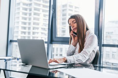 Busy day. Young woman in white formal clothes is indoors in the modern office.