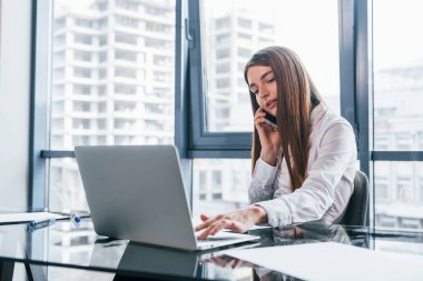 Busy day. Young woman in white formal clothes is indoors in the modern office.