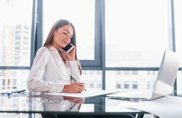 전화로 대화를 나누라 흰옷을 여자는 현대식 사무실에서 집안에 — 스톡 사진