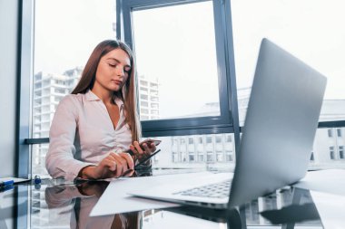 Busy day. Young woman in white formal clothes is indoors in the modern office.