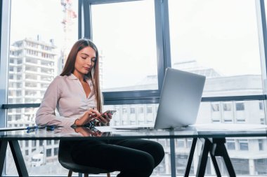 Busy day. Young woman in white formal clothes is indoors in the modern office.
