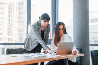 Laptop kullanıyorum. Modern ofiste resmi giyinmiş iki kadın birlikte çalışıyor..