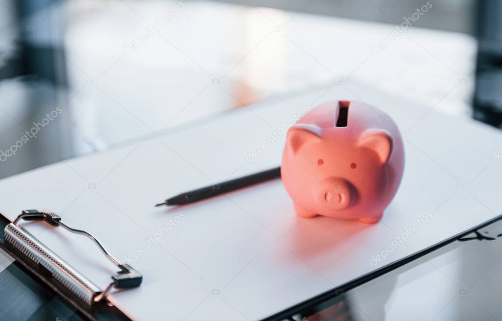 Close up view of pink piggy bank that lying on the white document on table.