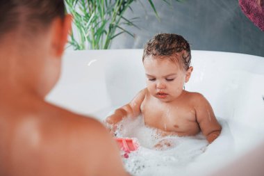 Two kids having fun and washing themselves in the bath at home.