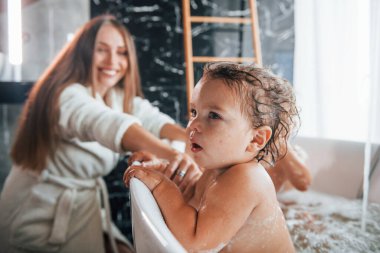 Young mother helps her son and daughter. Two kids washing in the bath.