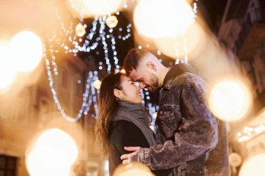 Artificial lighting by garlands. Happy multiracial couple together outdoors in the city celebrating New year.