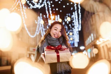 Hediye kutusuyla. Şehirdeki sevimli ve mutlu Asyalı genç bayan yeni yılı kutluyor..
