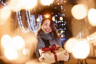 Hediye kutusuyla. Şehirdeki sevimli ve mutlu Asyalı genç bayan yeni yılı kutluyor..