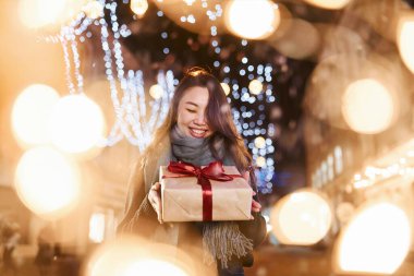 Hediye kutusuyla. Şehirdeki sevimli ve mutlu Asyalı genç bayan yeni yılı kutluyor..